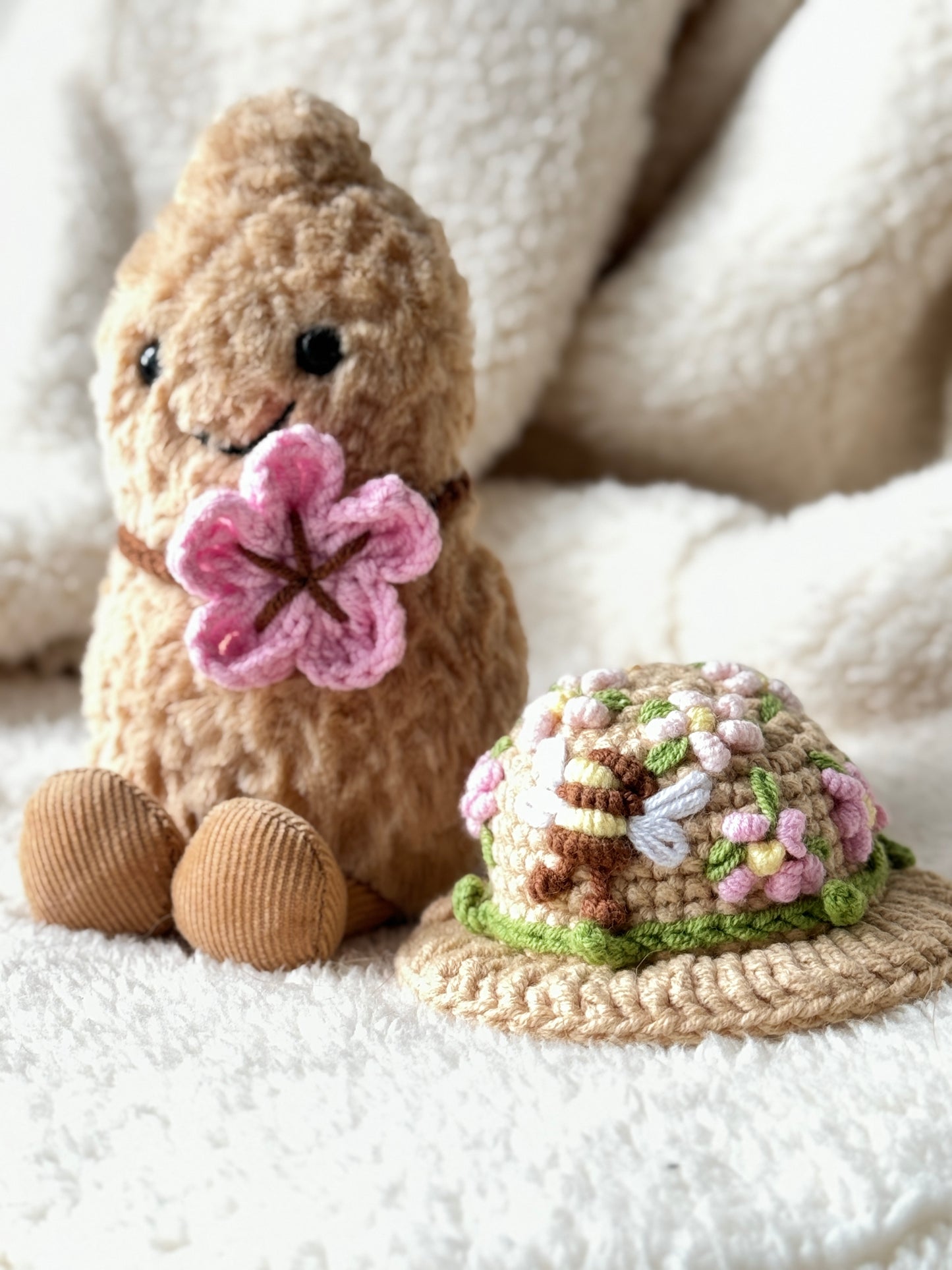 Crochet floral hat with embroidered flowers beside Jellycat Amuseable Peanut holding a pink crochet flower.