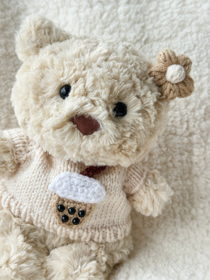 Close-up of crochet boba tea cup appliqué on cream knit Jellycat bear clothes — white foam, brown cup, black bead pearls
