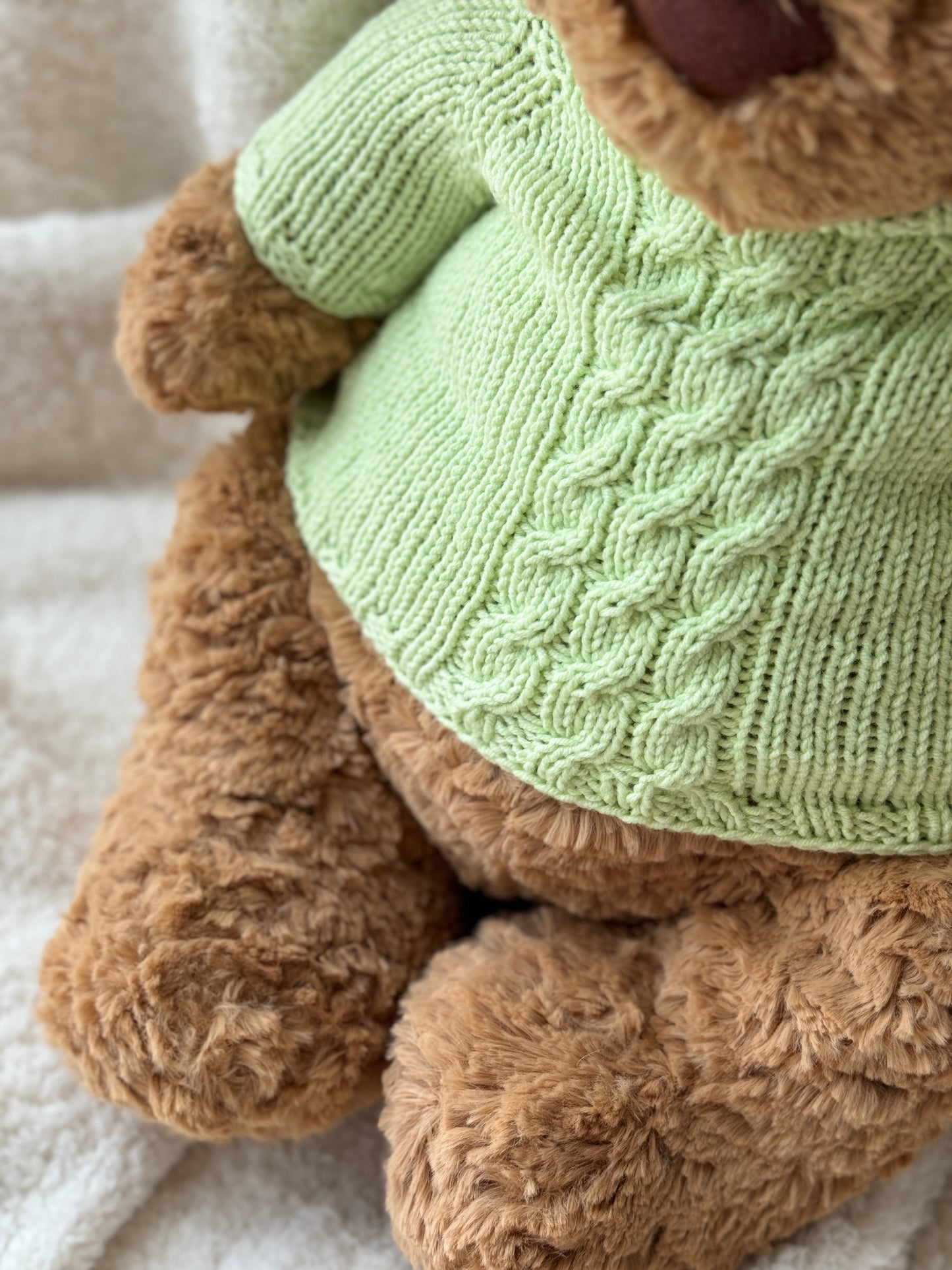 Close-up of Jellycat Bartholomew Bear wearing a green cable knit plush sweater with a fresh handmade style.