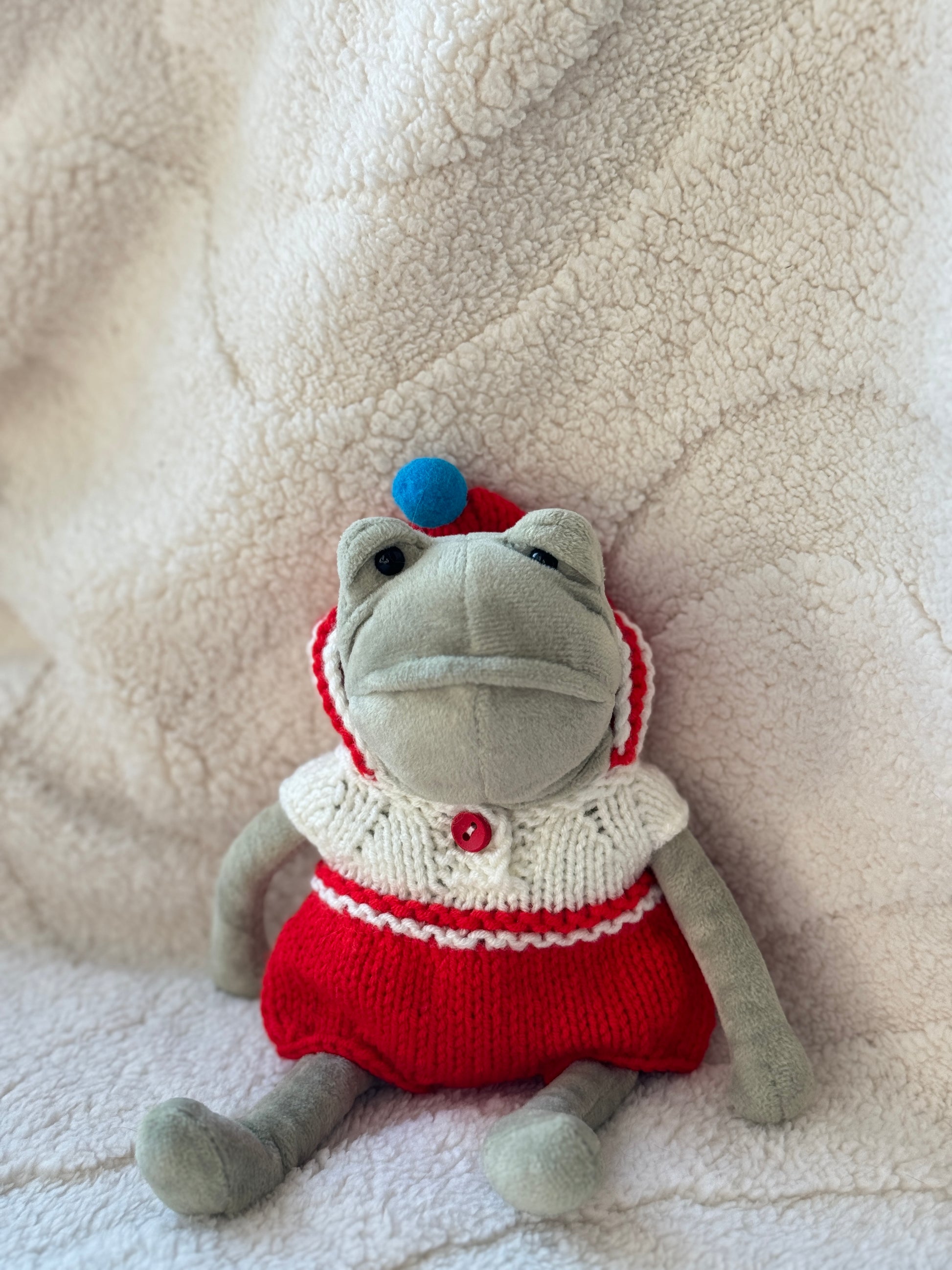 Jellycat Fergus Frog wearing handmade red and white knitted hooded romper with blue pom pom, front view