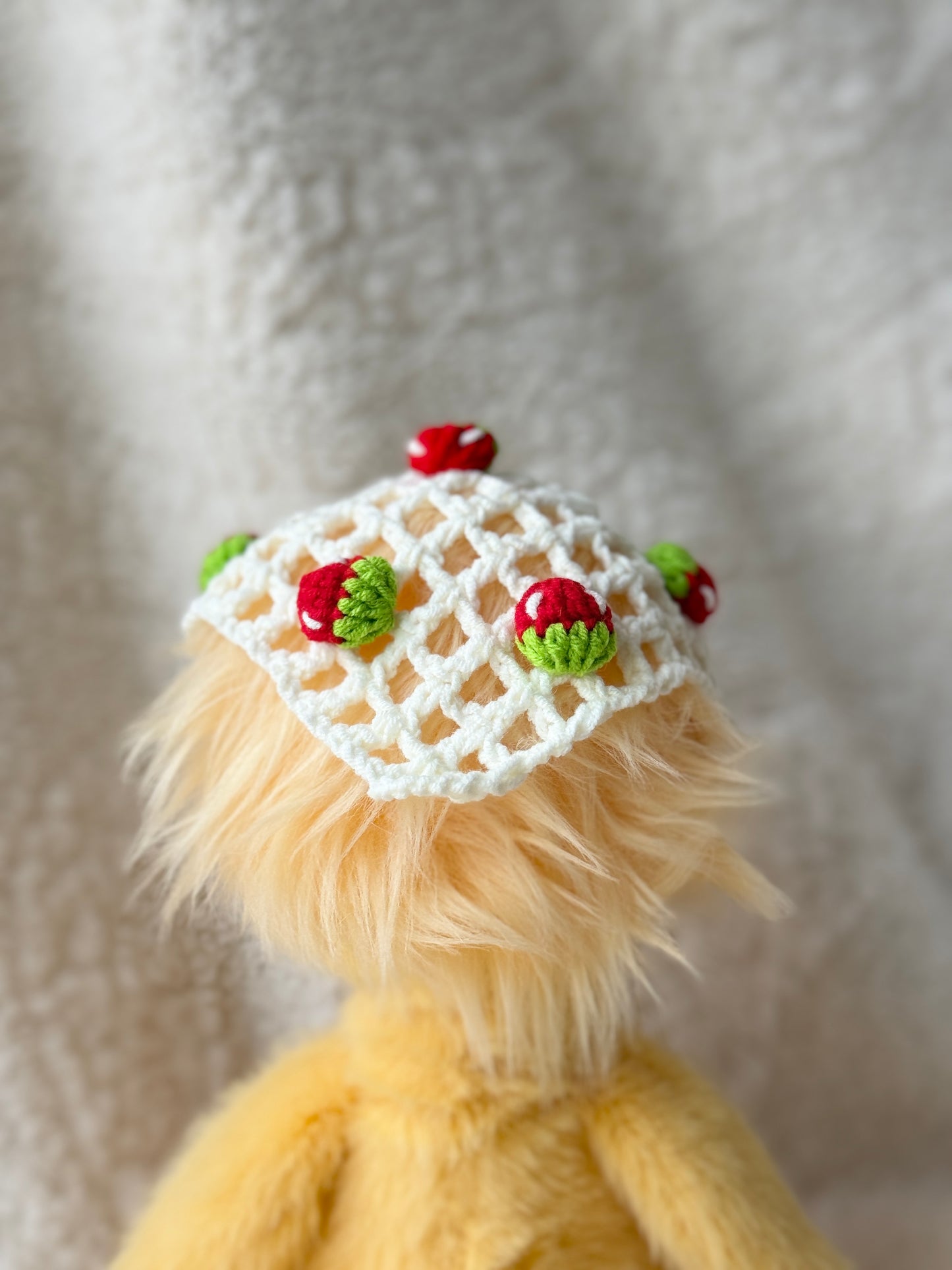 Back view of handmade crochet strawberry triangle bonnet for Jellycat Dorit Duck, showing the open lattice crochet pattern and small strawberry embellishments.
