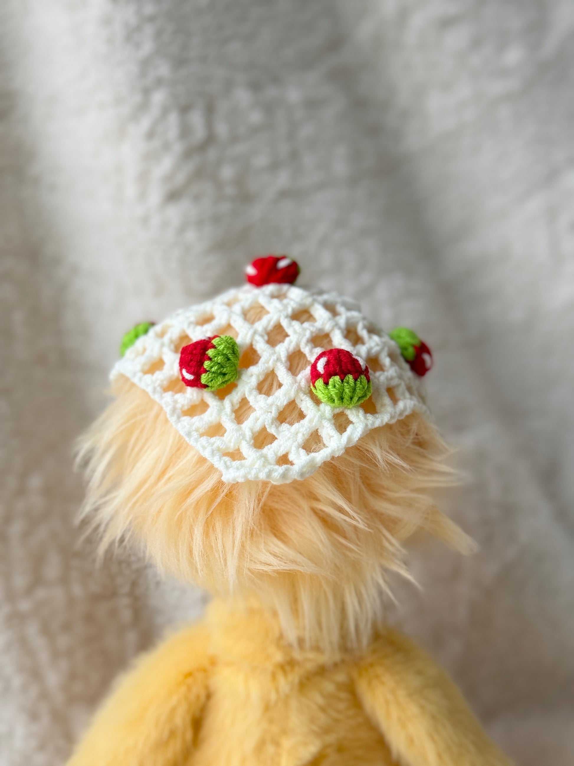 Back view of handmade crochet strawberry triangle bonnet for Jellycat Dorit Duck, showing the open lattice crochet pattern and small strawberry embellishments.
