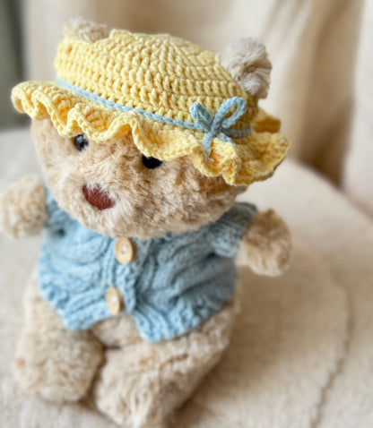 Close-up of Jellycat Bart Junior in a handmade yellow ruffle bonnet with pale blue bow detail and baby blue cardigan.