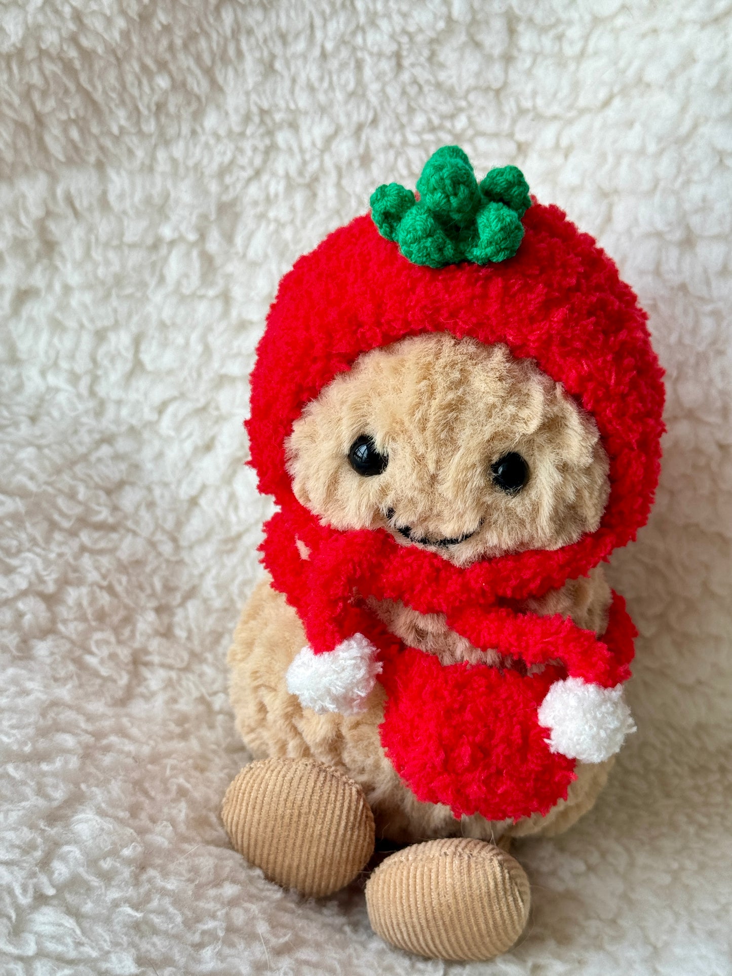 Close-up of handmade crochet tomato hat on Jellycat Peanut showing green sculpted leaf top detail and soft red chenille yarn texture