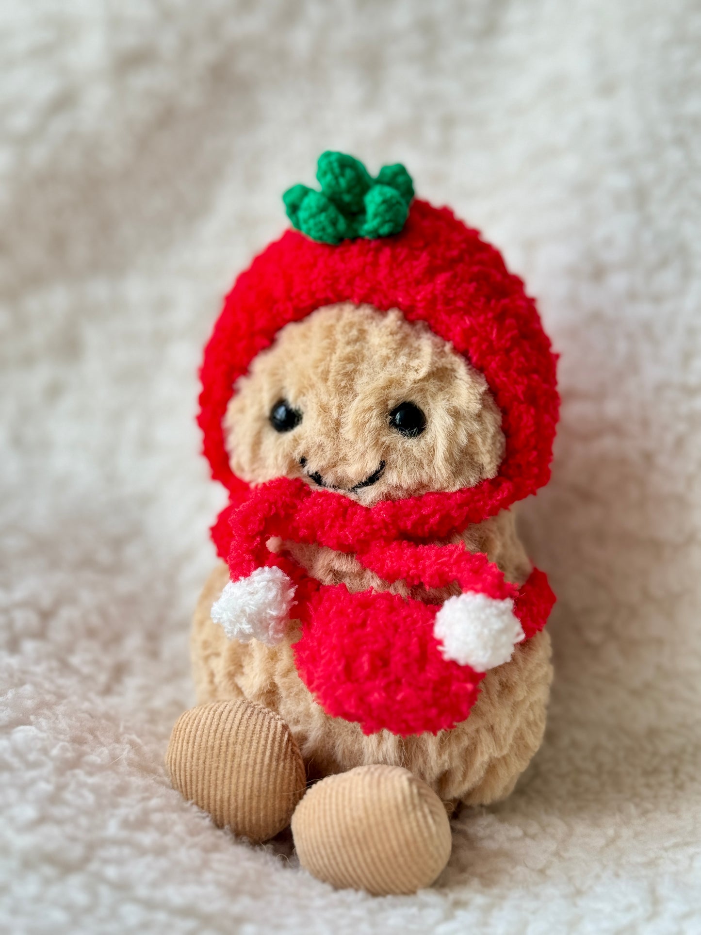Jellycat Peanut in full red crochet tomato outfit with white pompom scarf, front-facing display on fluffy white surface by Z Creations